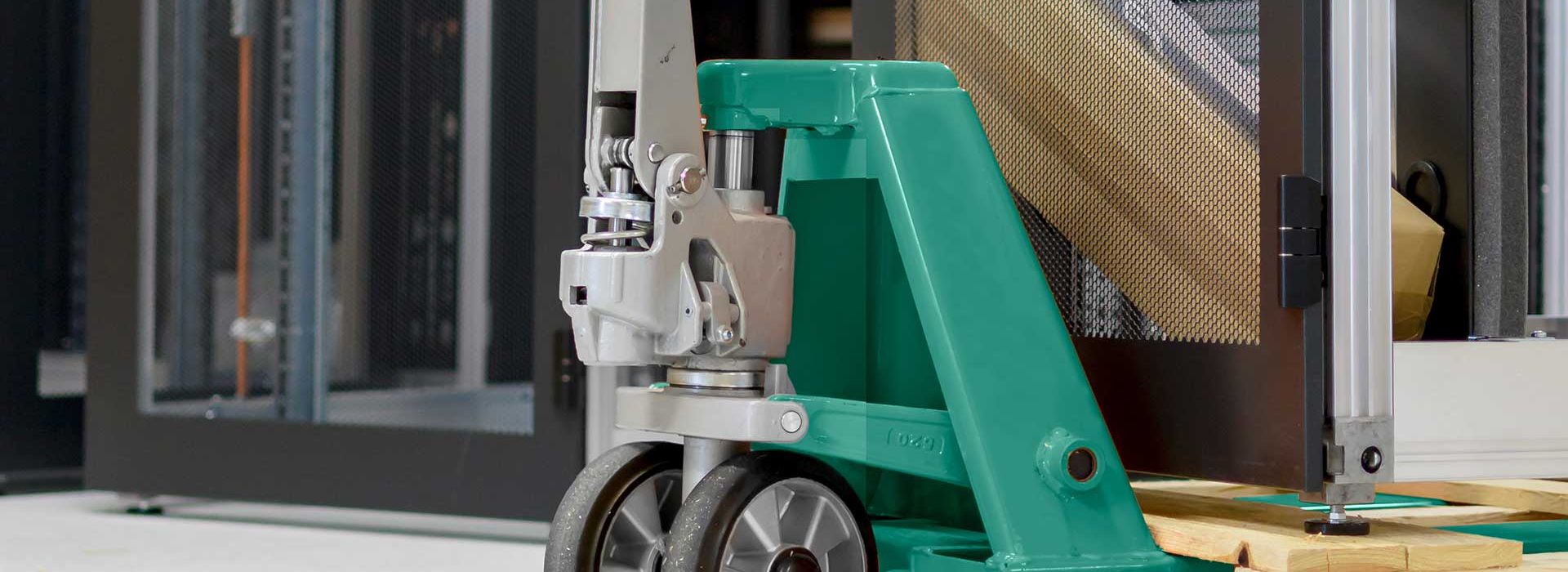 Ein Serverschrank steht auf einer Palette und wird mit einem Handhubwagen transportiert.