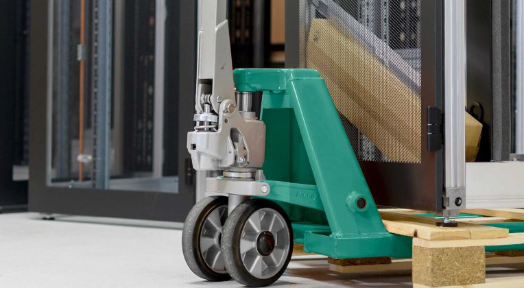 Ein Serverschrank steht auf einer Palette und wird mit einem Handhubwagen transportiert.